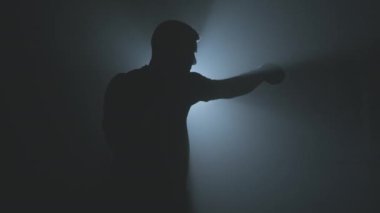 Karanlık spor salonunda boksör eğitiminin silueti. Gölge savaşı. Spor salonunda güçlü bir sporcu..