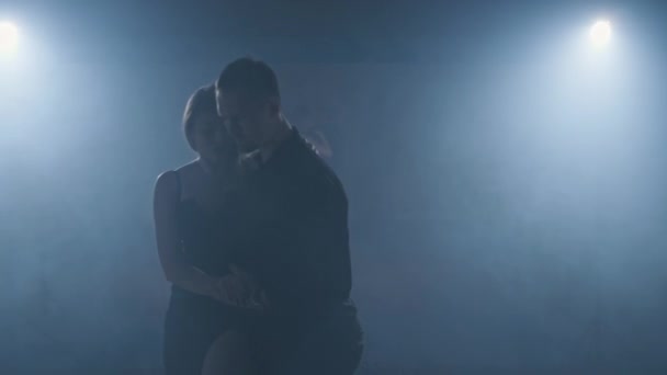Giovane coppia ballare tango in camera oscura con fumo e riflettori. Primo piano. — Video Stock