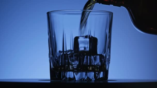 Whisky barman coulant en verre tournant à fond bleu. Gros plan en 4K — Video