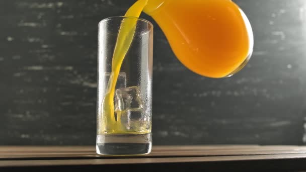 Despeje suco de laranja em vidro do jarro. Copo de suco de laranja com cubos de gelo — Vídeo de Stock