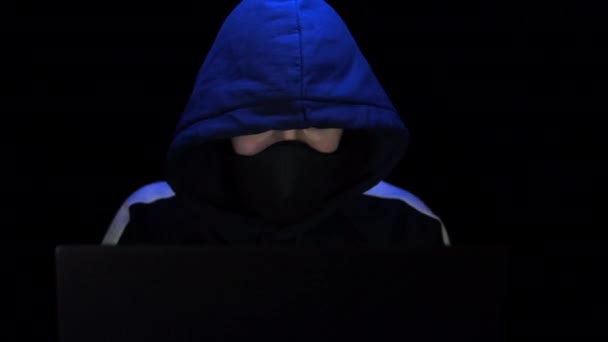 후드와 마스크를 쓴 남자 해커가 노트북에서 일하길 원했어요. 경찰 불빛 이 반사되다 — 비디오