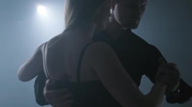 Genç çift karanlık odada dumanlı ve spot ışıklarıyla tango yapıyor. Dans eden çift