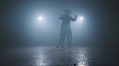 Genç çift karanlık odada dumanlı ve spot ışıklarıyla tango yapıyor. Geniş açı