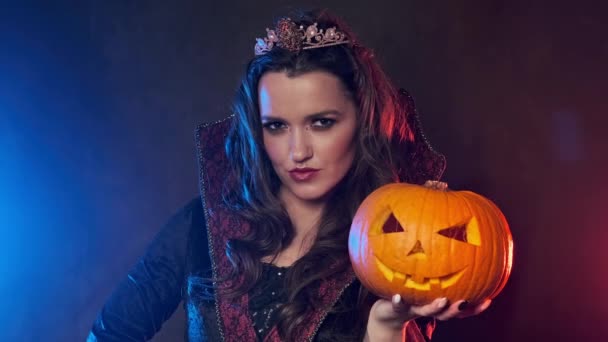 Young witch in cloak takes pumpkin. Beautiful female vampire in smoky studio — Stock Video