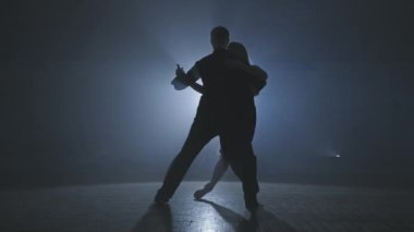 Dumanlı balo salonunda dansçıların silueti. Genç çift karanlık odada tango yapıyor.