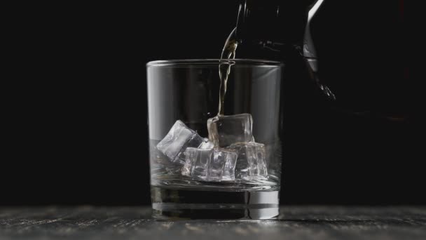 Alkohol nalévající sklenici z láhve. Zlatá whisky nalévání na černém pozadí — Stock video