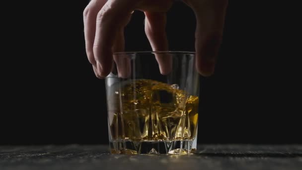 Hand hält Glas mit goldenem Whisky. Whiskey mit Eiswürfeln im Glas. — Stockvideo