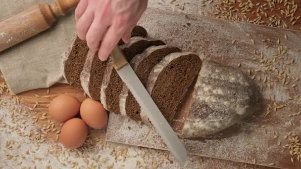 Trancher du pain sur une planche à découper en bois. Vue du dessus de la coupe du pain complet — Video