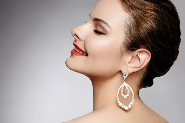 Hermosa mujer feliz en pendientes de moda de lujo. Diamante brillante joyería con brillantes. Sexy retrato de estilo retro. Modelo con accesorios glamour joyería y maquillaje labios de color rojo brillante — Foto de Stock