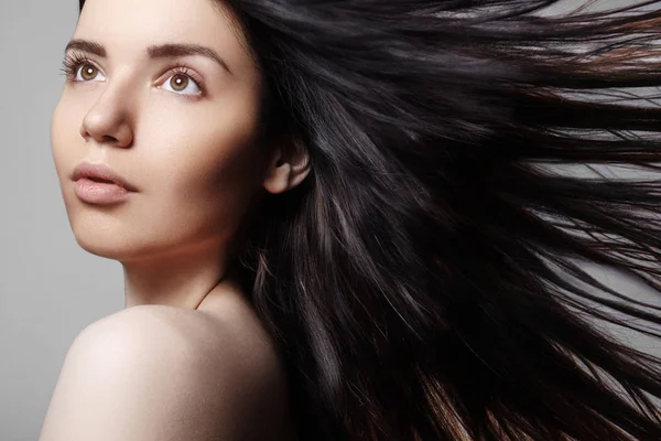 Wellness a spa. Krásná mladá žena model s větrem ošlehané hnědé vlasy na šedém pozadí. Vlasová kosmetika, kosmetika a wellness — Stock fotografie