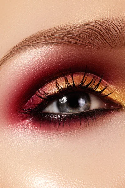 Ojo femenino de cerca con maquillaje brillante de moda. Hermoso oro, sombra de ojos roja, brillo, delineador de ojos negro. Forma cejas — Foto de Stock