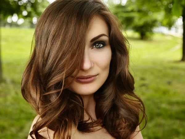 Close-up de jovem mulher bonita, em fundo de verão verde. Volume de cabelo e maquiagem de moda, pele limpa — Fotografia de Stock