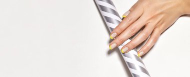 Geometrik arka planda parlak sarı Fransız manikürlü eller. Nails sanat tasarımı. Gümüş çizgili tüp üzerinde neon çiviler olan kadın ellerinin yakın çekimi. Boşluğu kopyala