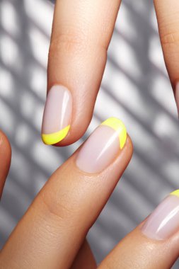 Geometrik arka planda parlak sarı Fransız manikürlü eller. Nails sanat tasarımı. Gümüş çizgili arka planda son moda neon tırnaklı kadın ellerinin yakın çekimi