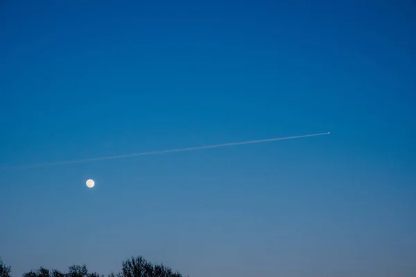 moon at sunset with a plane infront of it and a blue sky