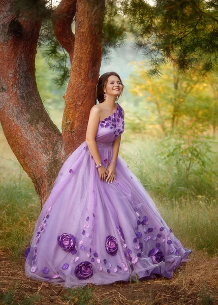 Beautiful girl in a gorgeous purple dress standing under a tree — Stock Photo, Image