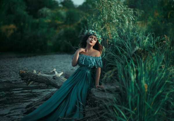 A big beautiful woman. The river witch casts a spell on the water. Green long dress, a wreath of herbs, a fabulous image.Fabulous image. Fashionable toning. Creative color.