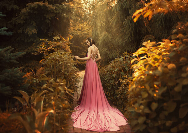 The Elf walks in the autumn garden. A girl with long ears in a beautiful pink dress with an open back and with a long train. Artistic processing