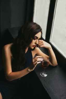 Gece elbisesi, zarif zarif kız styling - Hollywood dalga, makyaj dumanlı gözler ve kırmızı dudaklar. Bir bardak şarap cam kenarında olan üzgün kadın