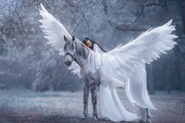 Elfo lindo e jovem, a andar com um unicórnio. Ela está usando um incrível vestido branco e leve. A rapariga deita-se no cavalo. Bela Adormecida. Fotografia artística — Fotografia de Stock