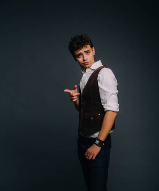 Bir gri studio arka plan üzerinde poz, genç, yakışıklı bir adam. Adam şık giyinmiş. Adam dikkat çağıran ve şaşkınlık ve iğrenme neden nesnede Puan bir parmak
