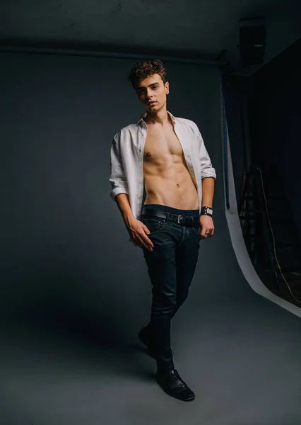 A young, handsome guy posing with an unbuttoned, white shirt, showing a sporty body, muscles, relief, pumped-up body. Background gray. Studio shooting, minimal, natural retouching — Stock Photo, Image