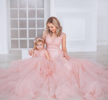 Anne ve kızı lüks, pembe, yeşil elbiseler. Aile kıyafetler, aynı elbiseler. Arka plan güzel, pahalı, beyaz, klasik iç kısmıdır. Sanat, aile fotoğraf