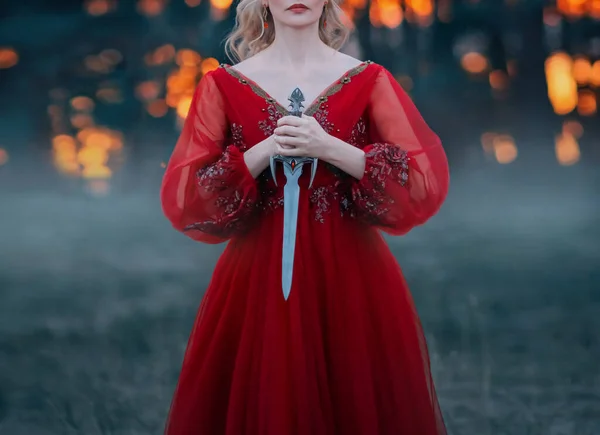 Una misteriosa mujer rubia sostiene una daga de hermoso diseño gótico en sus manos. Mujer soldado de fantasía guerrera de la moda en un bosque oscuro. Disparos sin rostro, solo labios y manos. Cortar la cabeza —  Fotos de Stock