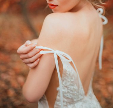 Elinle nazikçe dokun. Modaya uygun beyaz elbiseli, sırtı açık seksi, gizemli ve güzel bir kadının silueti. Yakın plan portre. Güzellik omuzlarını okşar. Turuncu dudaklar. sonbahar sanatı rengi.