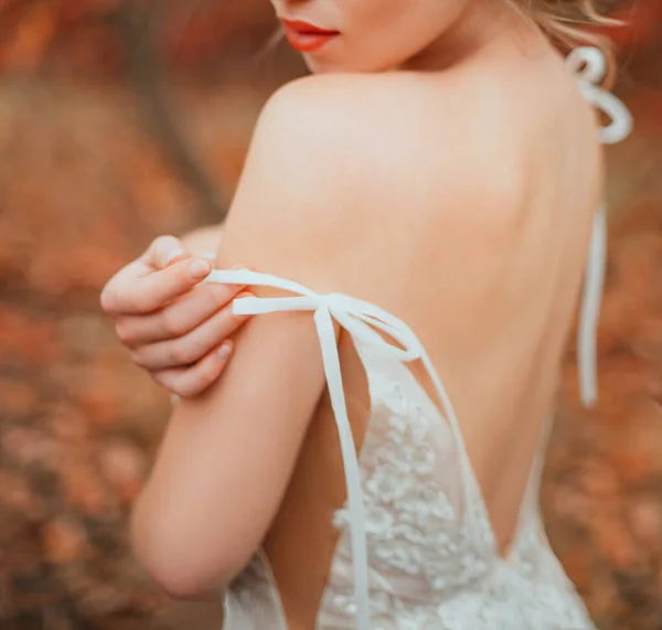 Tacto suave a mano. Silueta de una mujer misteriosa y hermosa en un vestido blanco de moda, con una espalda abierta y sexy. Retrato de cerca. belleza acaricia su hombro desnudo. Labios naranjas. otoño arte color . — Foto de Stock