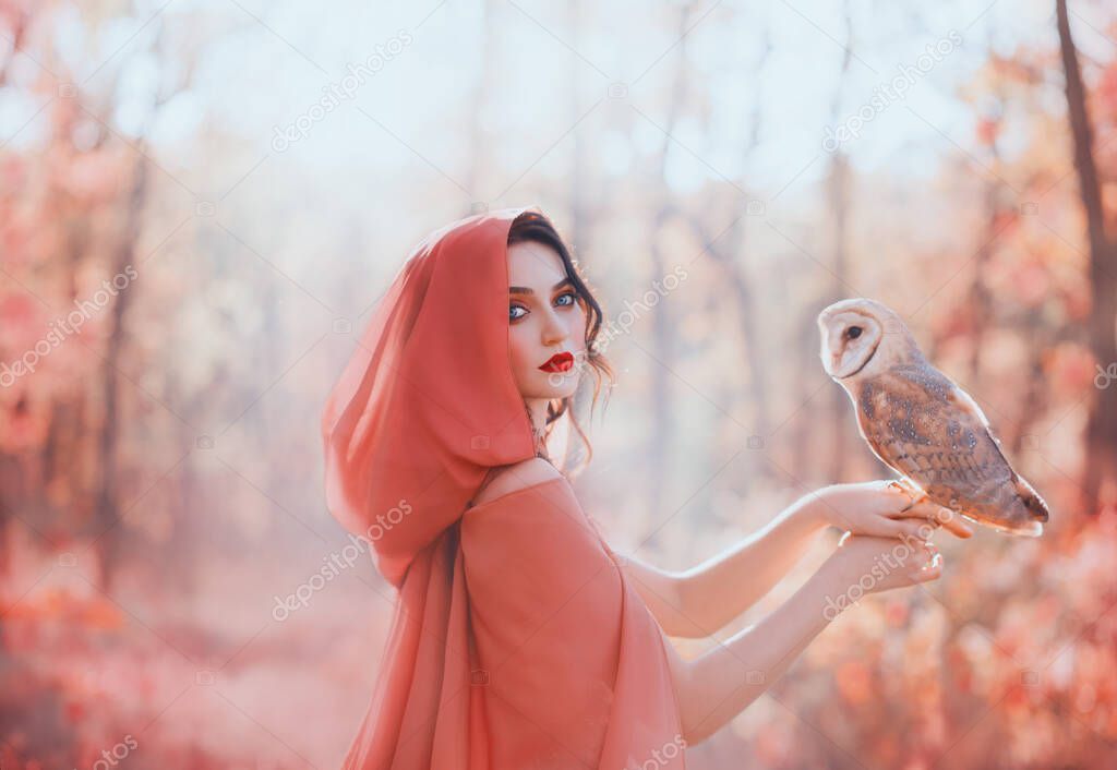 mystical pagan woman with covered head in peach scarf in forest, holds barn ow