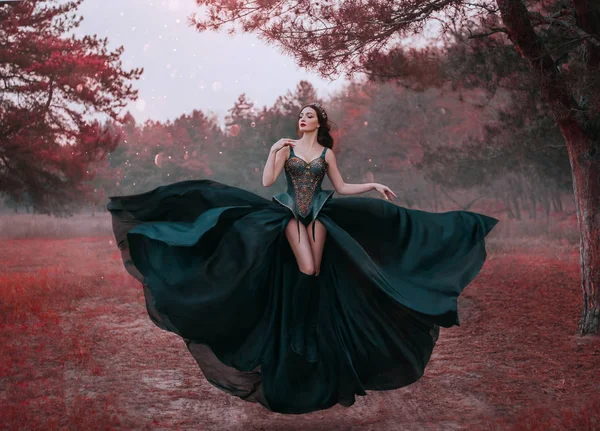 Belleza reina oscura en vestido creativo fantasía negro levita en el aire. Sexy diseño de corsé guerrero, piernas largas desnudas. Fondo bosque de otoño árboles rojos. falda de tela ondeando aleteo en el viento. Estilo de moda — Foto de Stock