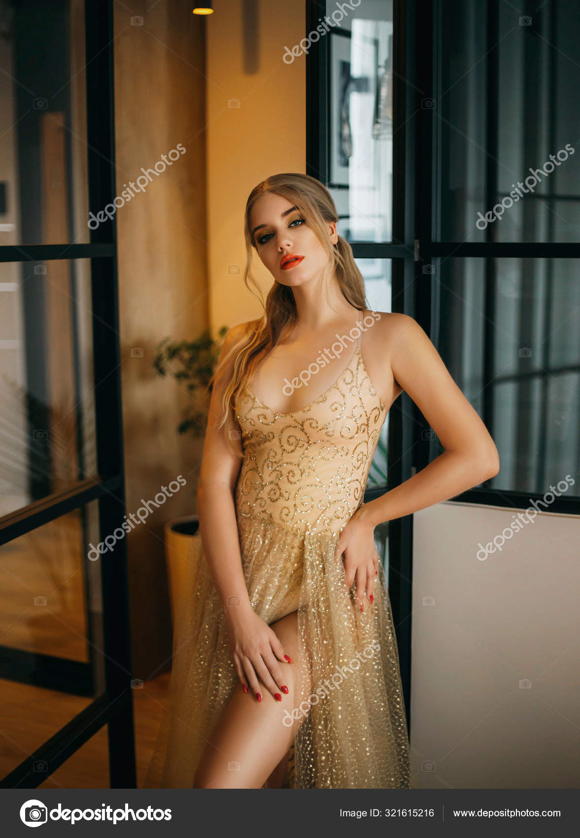 Stylish glamorous blonde woman in luxurious sparkling gold transparent dress.  Fashion style. Luxurious image for party. Evening outfit for the  graduation, Christmas, New Year. Background interior loft Stock Photo