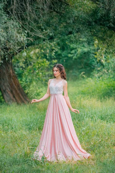 Roztomilá atraktivní brunetka žena těší přírodu v jemné elegantní růžové hedvábné šaty s bílou krajkou top. Obrázek pro slavnostní promoce ples stylové večerní oblečení oslavu. Módní glamor léto — Stock fotografie