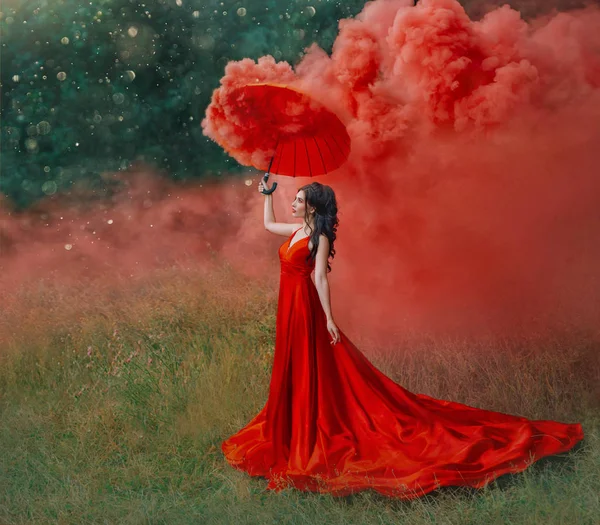 Kobieta w czerwonym jedwabiu długi pociąg sukienka z parasolem. Fotografia artystyczna. Idea Kreatywna sesja zdjęciowa z kolorowymi bombami dymnymi. Magiczna natura światła. Glamorous moda pani spacery w lesie. Walentynki — Zdjęcie stockowe