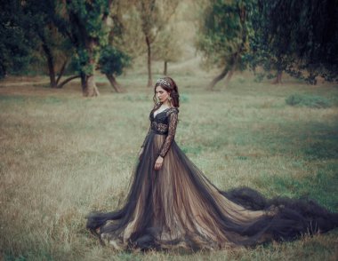 Bej renkli uzun trenli, lüks siyah elbiseli göz kamaştırıcı moda kadını. Arkaplan yaz doğası. Gotik fantezi güzellik kızı. Çekici seksi Karanlık Kraliçe. mezuniyet balosu için mezuniyet resmi