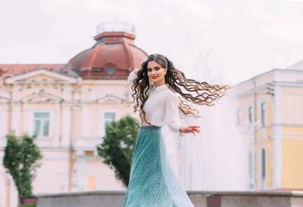 Brunetka studentka chodí tancovat, točí se venku po ulici. Dlouhé vlnité vlasy v pohybu. Veselá, šťastná holka. úsměv na tváři. bílá vinobraní halenka, mátová midi sukně. květinový tisk — Stock fotografie