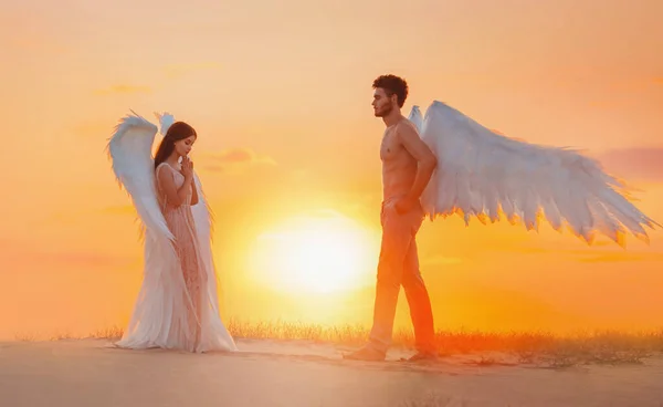 Dois anjos divinos, homem e mulher, vão ao encontro um do outro. Asas de fantasia branco design fantástico criativo. Menina com cabelo longo morena solta. Fundo brilhante pôr do sol ensolarado no fabuloso deserto de areia natural — Fotografia de Stock