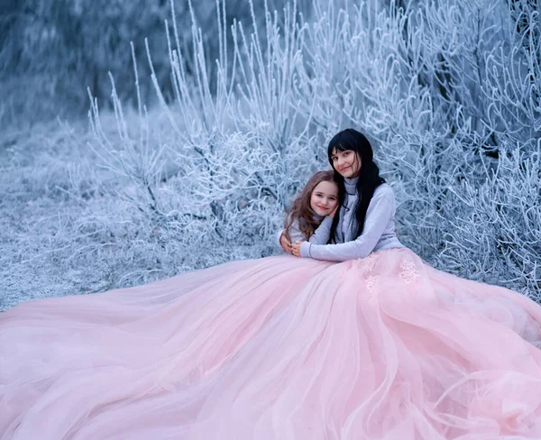 Närbild porträtt glad mamma kramar glad dotter på bakgrund vinter natur hes frost snö frost. Kvinna med långt svart hår brunett flicka. Familjen njuta av tystnad lyx lång puffy klänning varm blå tröja — Stockfoto