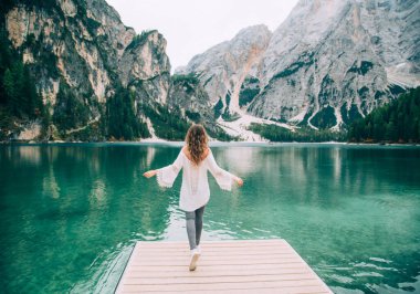 Uzun saçlı romantik kız, arkasını döndü, ahşap iskele Braies 'e uzandı. Turistler esrarengiz doğanın tadını çıkarırlar Yeşil ormanlı Alp dağları berrak su sessizliği