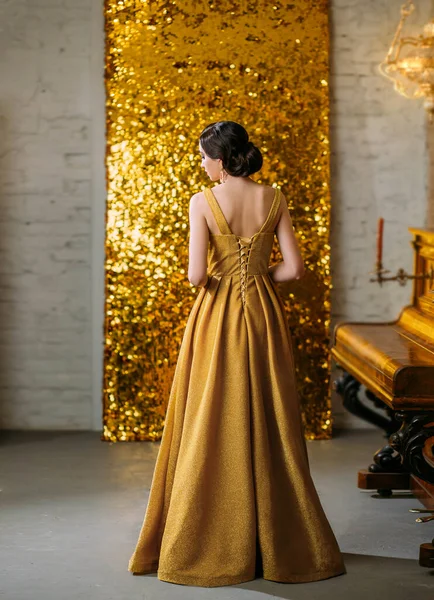 Young retro beautiful Great Gatsby woman turned stands backdrop sparkling golden screen piano. Brunette with finger wave hairstyle in classic elegant dress vogue fashion style 1920. Christmas ball — Stock Photo, Image