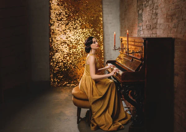 Young woman with finger wave hairstyle gold dress vogue fashion old style 1920 play piano candles romantic burning. Retro Great Gatsby backdrop shine sparkle room brick wall. Musician graduate party — Stock Photo, Image