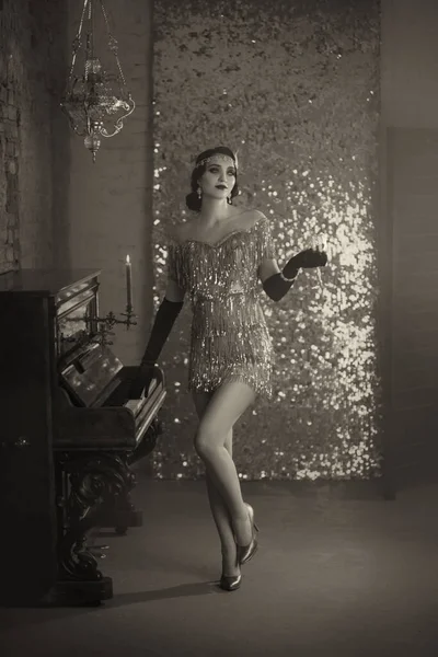 Siyah ve beyaz retro kadın. Parmak dalgası saç stili, kısa kaliteli gümüş renkli parlak elbise tarzı 20 'ler. Kız eski piyanonun yanında duruyor. Arkaplan romantik klasik iç mekan parlak parıltı duvar, yanan mum