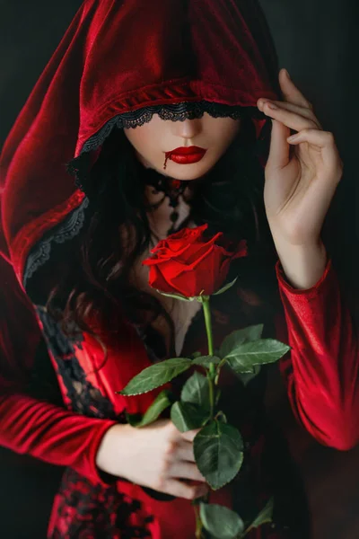 Μυστηριώδης τρομακτική σιλουέτα όμορφη γοτθική γυναίκα στο καπό. Κόκκινα χείλη βαμπίρ που στάζουν αίμα. Γυναίκες αντιμετωπίζουν ματωμένο μακιγιάζ από κοντά. Μόδα Απόκριες σχέδιο τέχνης. σέξι γυναικείο βελούδινο φόρεμα. κρατήστε το πλήρες τριαντάφυλλο — Φωτογραφία Αρχείου