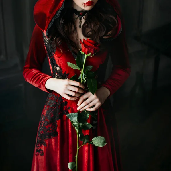 Retrato de primer plano silueta gótica sexy mujer vampiro místico. Vestido largo de lujo, campana. Collar vintage. Reina medieval sostiene rosa roja en las manos. pelo ondulado negro. Maquillaje de Halloween festivo, gotas de sangre —  Fotos de Stock