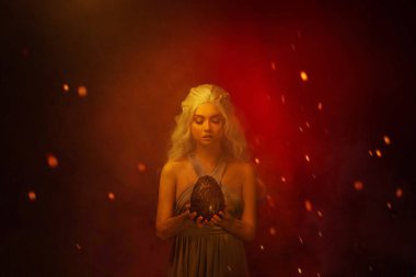 Sanat portresi genç, güzel, sarı saçlı, kül lekeli yüzü olan bir kadın. Fantezi kraliçesi mistik ejderha yumurtası tutuyor. Arkaplanda karışık neon ışıklı kırmızı kıvılcımlar tütüyor. Cadılar Bayramı Resmi 