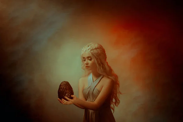 Художественная королева в огне. Сказочная таинственная молодая красивая блондинка принцесса выглядит с любовью фантазии надежды сказка древний старый яйцо дракона. Фон светло-красный дым. симпатичная греческая модель — стоковое фото