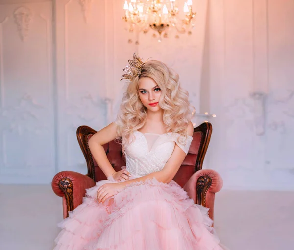 Charming beautiful delightful young girl princess sitting in antique vintage armchair waiting fairy miracle. Queen woman smiles mysteriously cute. Blonde long curly hair. Delicate pink airy sexy dress — Stock Photo, Image