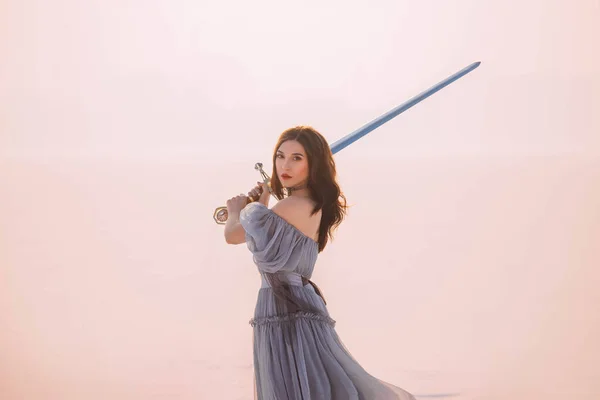 Retrato de arte jovem bela mulher guerreira corajosa princesa. Rainha medieval detém aço prata espada mágica. Conceito Liberdade de proteção. longo cabelo retro vestido azul cinza vintage. Inverno branco neve natureza — Fotografia de Stock