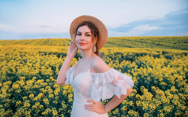 Porträtt ung glad rustik retro kvinna. Halmvintagehatt. Vit lyxig brudklänning. Bakgrund blommande gula våren blommor raps fält. Ljus sommarhimmel. Naturlig makeup. Härligt leende ansikte — Stockfoto